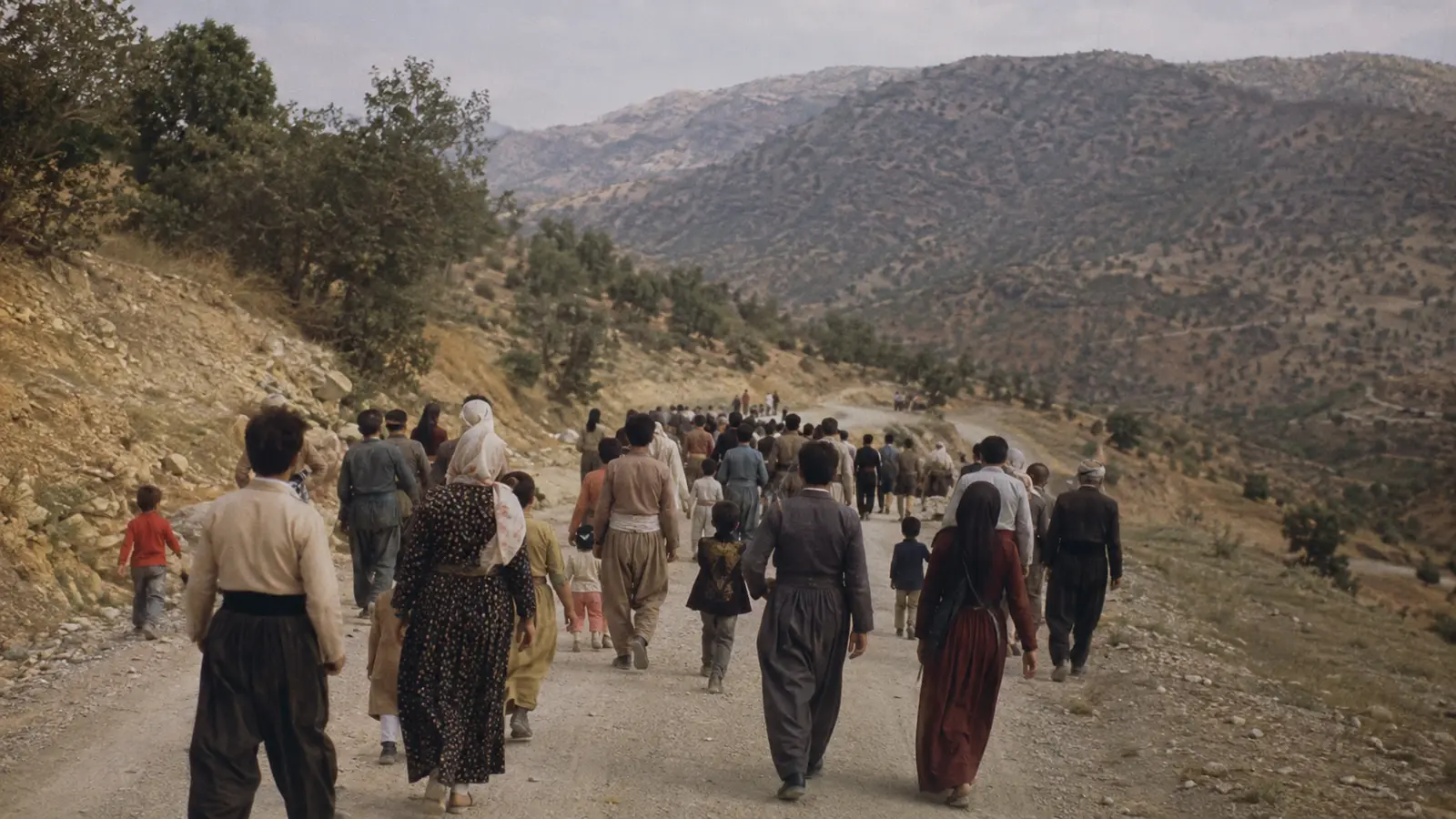 گروهی از مردم در حال حرکت در جاده‌ای کوهستانی در کردستان