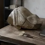 پارچە پەیکەرێکی کۆن و شکاو لەسەر مێزی کارگەی چاککردنەوەی مۆزەخانە